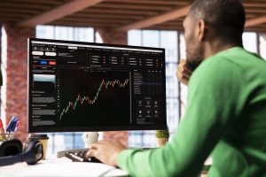 Day trader using computer, purchasing stocks that might perform well and selling ones that might drop in value. Forex trader browsing though stock exchange portfolio pages at PC desk