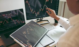Investor man analyzing the graph of the stock market using a pen pointing to the computer screen.
